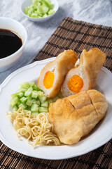 Indonesian pempek kapal selam filled with boiled egg yolk, served with noodles, cucumber, and vinegar sauce. A delicious traditional Palembang dish on a white plate with natural garnish