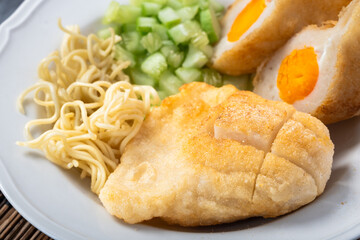 Close-up of Indonesian pempek with salted egg filling, served with diced cucumber and noodles. A savory traditional dish from Palembang, showcasing rich texture and golden crust