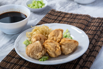 Close-up of traditional Indonesian fried pempek served with yellow noodles, chopped cucumber, and...