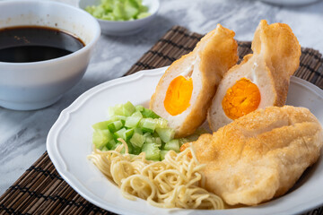 Indonesian pempek kapal selam filled with boiled egg yolk, served with noodles, cucumber, and...