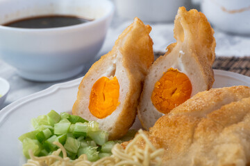 Indonesian pempek kapal selam filled with boiled egg yolk, served with noodles, cucumber, and vinegar sauce. A delicious traditional Palembang dish on a white plate with natural garnish