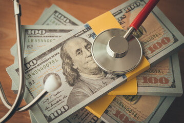 Stethoscope on stack US dollar banknotes with wooden table background. Savings for cost of medical...