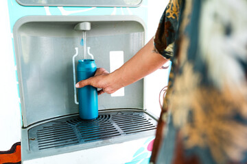 Refillable water bottle being filled at eco-friendly hydration station. Close-up of hand refilling...