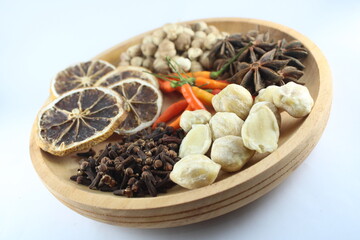 Cardamom, cloves, star anise, dried lemon, candlenut, and chili peppers arranged in a wooden bowl...