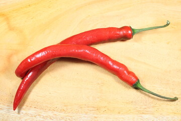 Two fresh red chili peppers placed on a light wooden surface. Perfect for food styling, spicy...