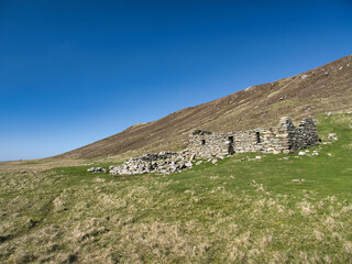 An abandoned stone cottage set against rolling hills in Collaster, Unst, Shetland.
