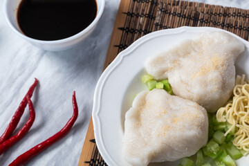 Traditional Indonesian pempek served with diced cucumber, yellow noodles, and spicy vinegar sauce on the side. A savory delicacy made from fish and tapioca