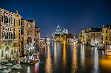 Night view of the Grand Canal in Venice, Italy, with historic buildings and Santa Maria della Salute basilica illuminated and reflected in the water.