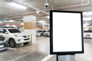 Blank signage board in underground parking garage with blurry cars and concrete pillars in background for mockup