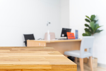 Empty wooden table with blurred modern office background, computer desk, and indoor plant in clean workplace