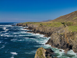 The rugged coastline of West Unst near Newgord, Shetland, showcases dramatic cliffs against a vibrant blue sea.
