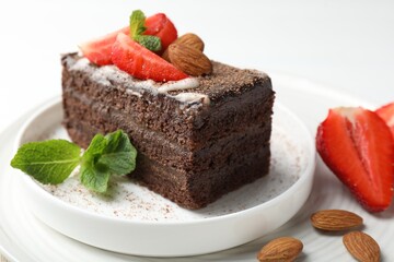 Piece of delicious chocolate cake with strawberries, almonds and mint on table, closeup
