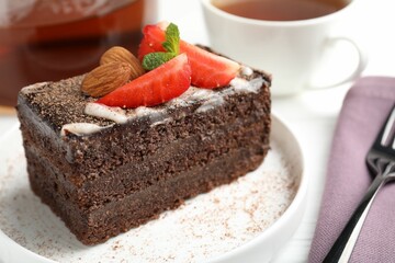 Piece of delicious chocolate cake with strawberry, almonds and tea on table, closeup