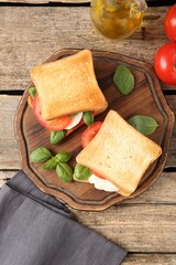 Tasty sandwiches with mozzarella cheese, tomatoes and basil on wooden table, flat lay