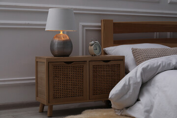 Bedside table with lamp and alarm clock near bed indoors
