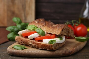 Tasty sandwich with mozzarella cheese, tomatoes and basil on wooden table, closeup