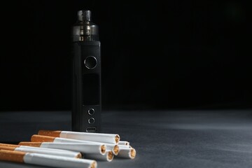 Electronic smoking device and cigarettes on dark table against black background, closeup. Space for...
