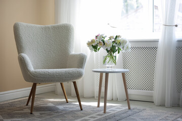 Comfortable armchair and table with vase of flowers near window indoors. Interior design