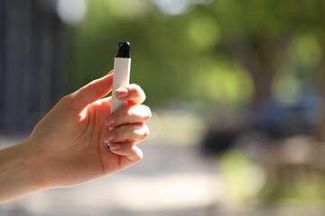 Young woman with electronic smoking device outdoors, closeup. Space for text