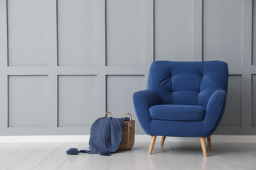 Comfortable blue armchair and basket with cloth near light grey wall indoors, space for text