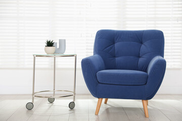 Comfortable blue armchair and side table near white wall indoors