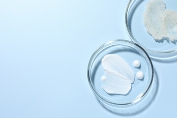 Different cosmetic products in Petri dishes on light blue background, flat lay. Space for text
