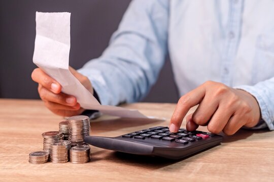 A woman holding a shopping receipt paper and calculating the expenses using calculator