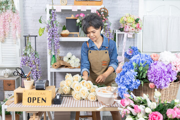 Asian senior woman, florist, small business, owner arranging roses at flower shop table, expressing creativity, passion, cheerful lifestyle, floral service and retirement independence, aging lifestyle