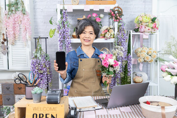 Asian senior woman, florist, small business, owner holding bouquet and smartphone in flower shop, presenting service, digital marketing confidence, and floral, modern aging people with technology