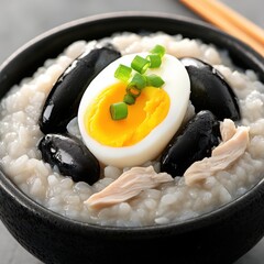 A bowl of congee rice porridge topped with scallions, century egg, and shredded chicken, soft morning light