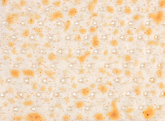 Close-up texture of traditional matzo reveals its golden-baked surface and tiny perforations,...