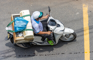 A man carries a complete air conditioner on a motorcycle along a city street, Vietnam
