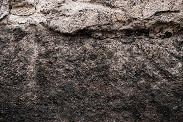 Close-up of a rough, weathered stone wall featuring layered textures and earthy tones of brown, black, and gray with natural surface erosion