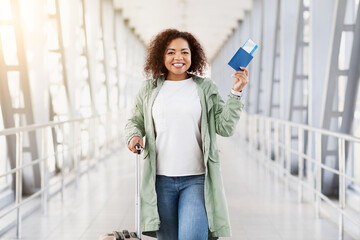 Ready For Trip. Smiling young Black woman at airport holding passport and ticket, joyful and...
