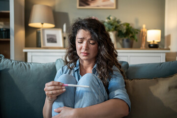 Sad woman looking at negative pregnancy test sitting on sofa at home