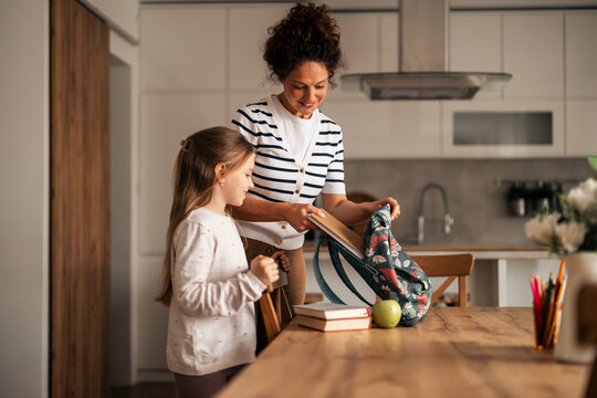 Mother Preparing Daughter’s Backpack for School in Modern Kitchen Setting