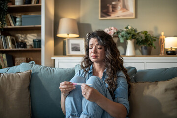 Sad woman holding negative pregnancy test sitting on sofa at home