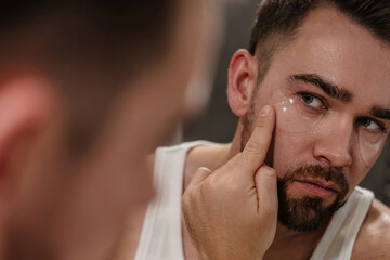 Man applying under eye patches in front of a bathroom mirror