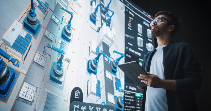 Indian Robotics Specialist Programs a Group of Robotic Arms with the Help of a Tablet Computer. Specialist Creates and Programs the Assembly Line Online, Optimizing Production and Improving Efficiency - Powered by Adobe