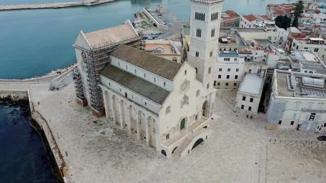 Aerial drone view of Trani, a coastal town in Puglia, Italy, featuring the iconic Trani Cathedral, Castello Svevo, picturesque harbor, and Adriatic Sea shoreline under clear skies.