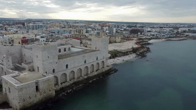 Aerial drone view of Trani, a coastal town in Puglia, Italy, featuring the iconic Trani Cathedral, Castello Svevo, picturesque harbor, and Adriatic Sea shoreline under clear skies.