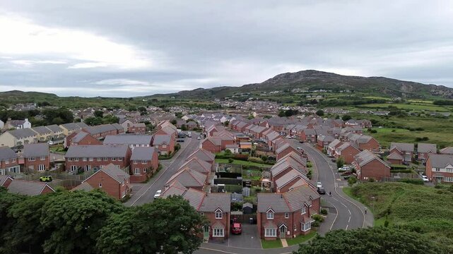 Aerial view flying across modern red brick housing neighbourhood under Holyhead mountain in Wales