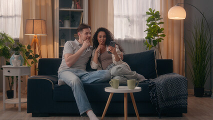 Smiling multiracial couple multiethnic Caucasian man male guy husband with Hispanic woman female girl wife shopping mobile phone together talking discuss interior furniture order smartphone at home