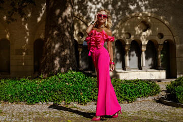 Elegant fashion model in a bold fuchsia feather jacket and jumpsuit with ruffled top and heels...