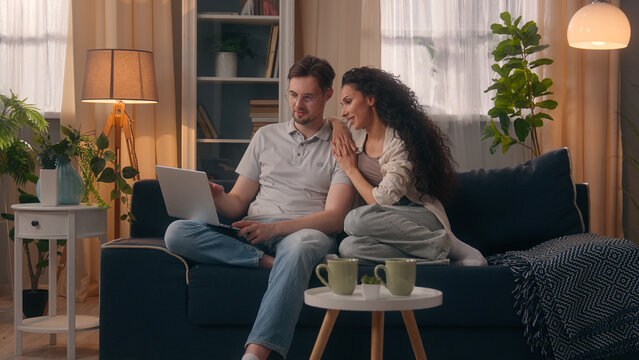 Smiling happy multiracial couple multiethnic Caucasian man male guy husband boyfriend with Hispanic Latina woman female girl wife girlfriend shopping computer together talking discuss laptop at home