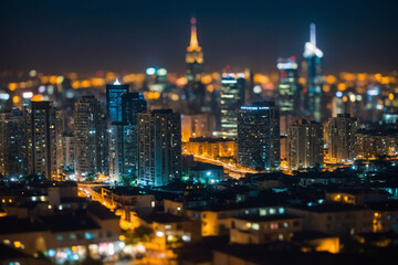A wide-angle nighttime cityscape showing out-of-focus urban lights creating a soft gradient of color and brightness over silhouetted structures, background details remain identifiable