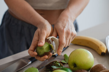 Woman Peeling Fresh Kiwi Fruit in Kitchen with Apples and Banana Nearby