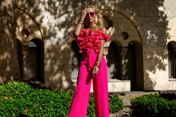 Elegant fashion model in a bold fuchsia feather jacket and jumpsuit with ruffled top and heels...