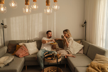 Couple sharing a plate of French fries and chicken nuggets  in cozy lving room