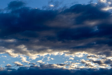 Dramatic sky features layers of dark, heavy clouds interspersed with patches of bright, illuminated...
